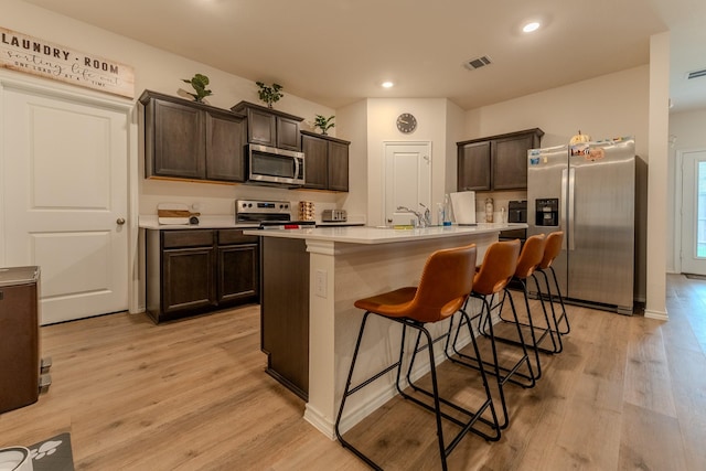 kitchen featuring light countertops, stainless steel appliances, dark brown cabinetry, and light wood-style floors