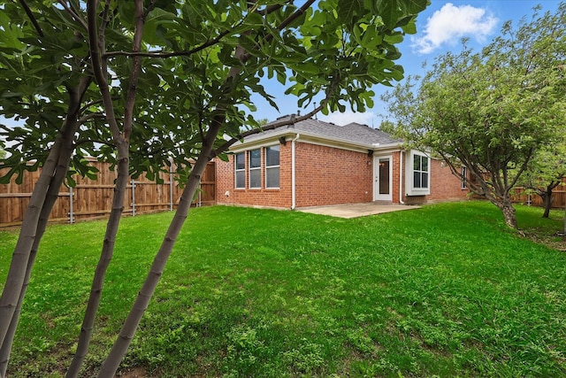 back of property featuring roof with shingles, a lawn, brick siding, a fenced backyard, and a patio