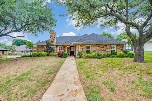 ranch-style house featuring brick siding, a chimney, a shingled roof, and a front yard