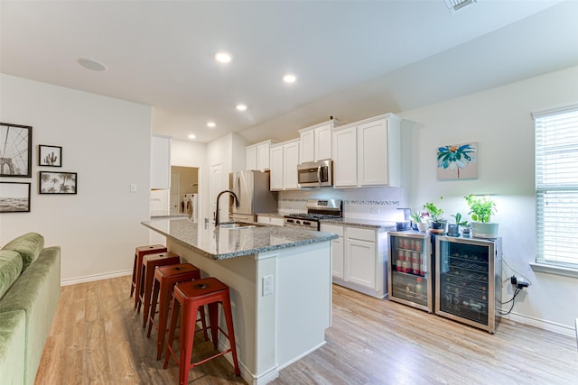 kitchen with washer and dryer, a breakfast bar, an island with sink, light wood-type flooring, and stainless steel appliances