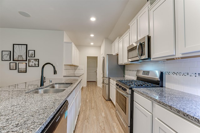 kitchen with appliances with stainless steel finishes, light stone countertops, light wood-type flooring, a sink, and white cabinets