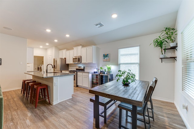 kitchen with visible vents, appliances with stainless steel finishes, light wood-type flooring, white cabinets, and an island with sink