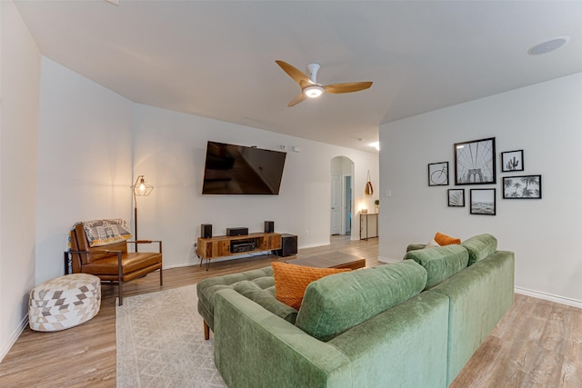 living room featuring arched walkways, ceiling fan, baseboards, and light wood-style flooring