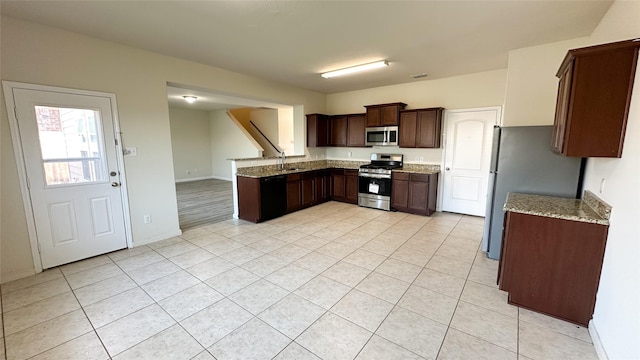 kitchen with dark brown cabinetry, light tile patterned floors, light stone counters, baseboards, and stainless steel appliances