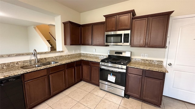 kitchen with dark brown cabinetry, a sink, light stone counters, light tile patterned floors, and stainless steel appliances