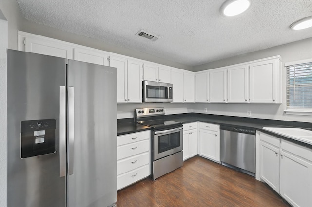6317 N Park Dr, Watauga, TX 76148 - kitchen with a textured ceiling, visible vents, dark countertops, appliances with stainless steel finishes, and white cabinets