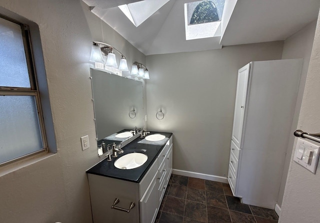full bath with double vanity, stone finish flooring, a skylight, a sink, and baseboards