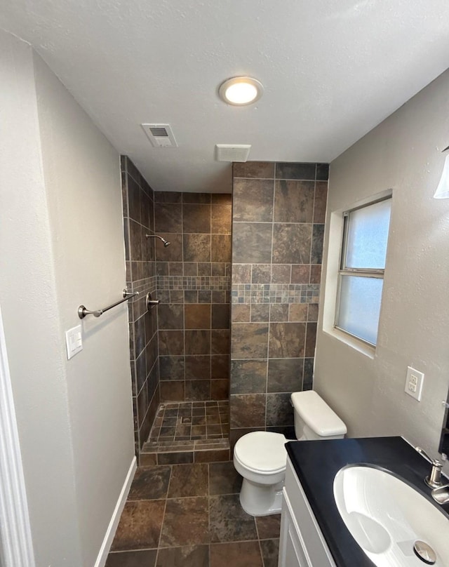 bathroom featuring a tile shower, vanity, toilet, stone finish flooring, and visible vents