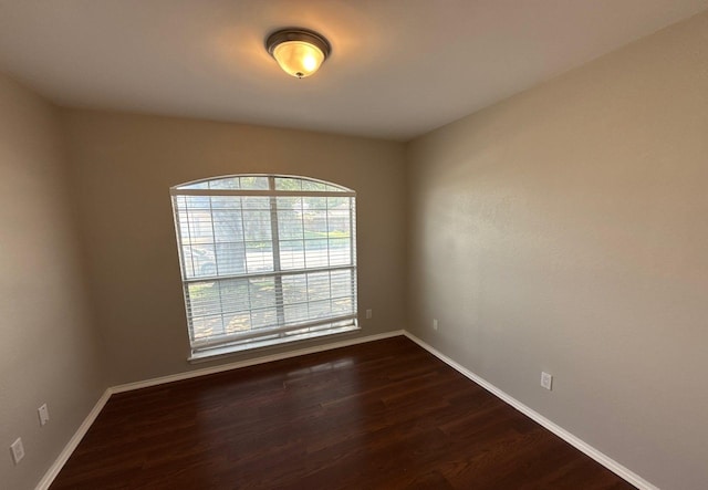 spare room with baseboards and dark wood-style flooring