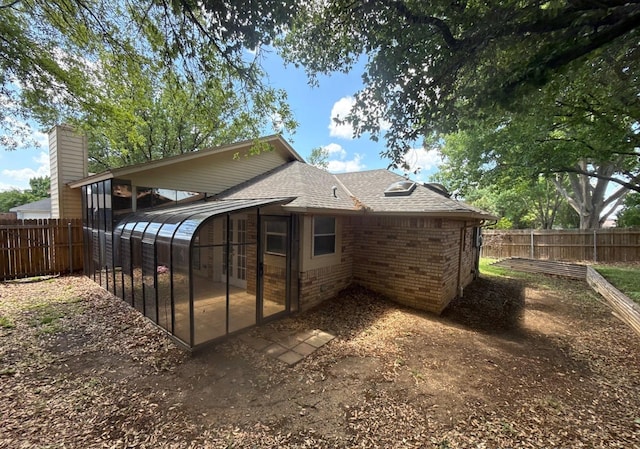 back of property featuring a sunroom, a fenced backyard, roof with shingles, and brick siding