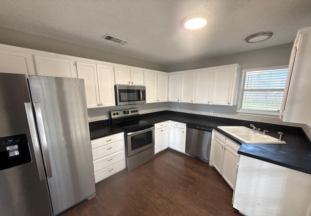 kitchen with dark wood-style flooring, appliances with stainless steel finishes, dark countertops, a sink, and white cabinets