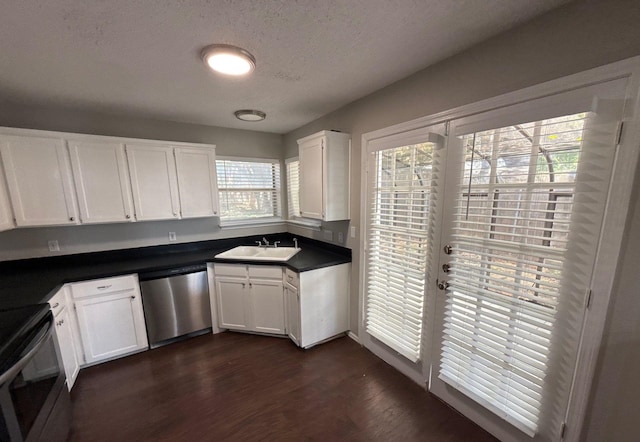 kitchen featuring dark wood-style flooring, dark countertops, white cabinets, a sink, and stainless steel appliances