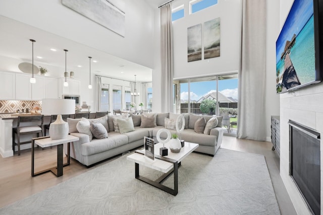 living area featuring a fireplace, recessed lighting, a high ceiling, and light wood-style floors