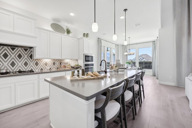 kitchen with decorative backsplash, white cabinets, appliances with stainless steel finishes, and a center island with sink