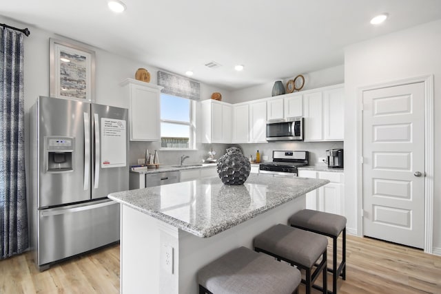 kitchen with white cabinets, appliances with stainless steel finishes, a sink, light wood finished floors, and visible vents