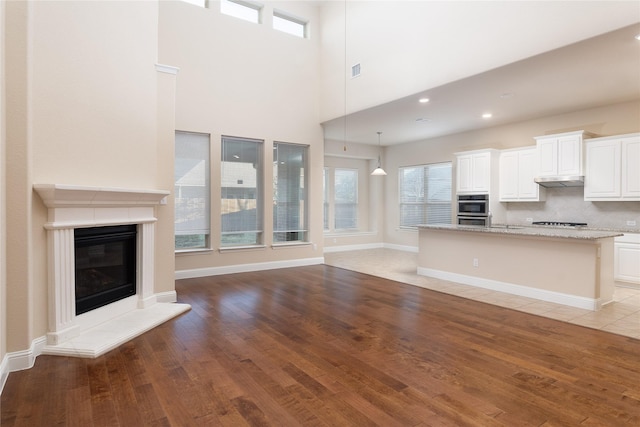 5201 Dallas Red Ct, Mckinney, TX 75070 - unfurnished living room with a high ceiling, light wood finished floors, a glass covered fireplace, baseboards, and visible vents