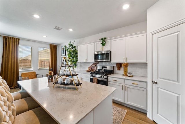 859 Sitwell Dr, Fate, TX 75087 - kitchen with backsplash, visible vents, appliances with stainless steel finishes, a center island, and light wood finished floors