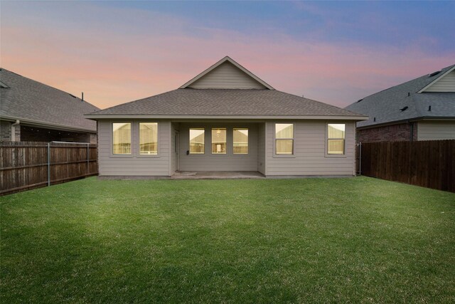 859 Sitwell Dr, Fate, TX 75087 - back of property at dusk with a lawn, a fenced backyard, and roof with shingles