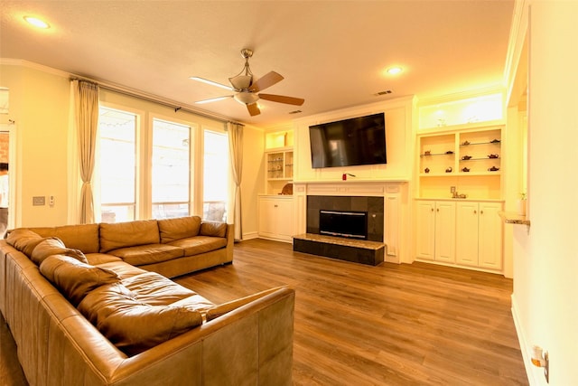 living area with ceiling fan, a tiled fireplace, crown molding, wood finished floors, and baseboards