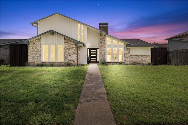 mid-century inspired home featuring fence, a chimney, a yard, and brick siding