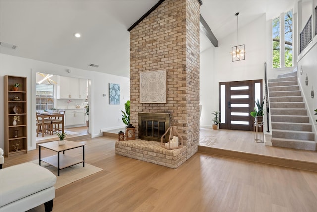 living area featuring visible vents, light wood-style flooring, a chandelier, and high vaulted ceiling