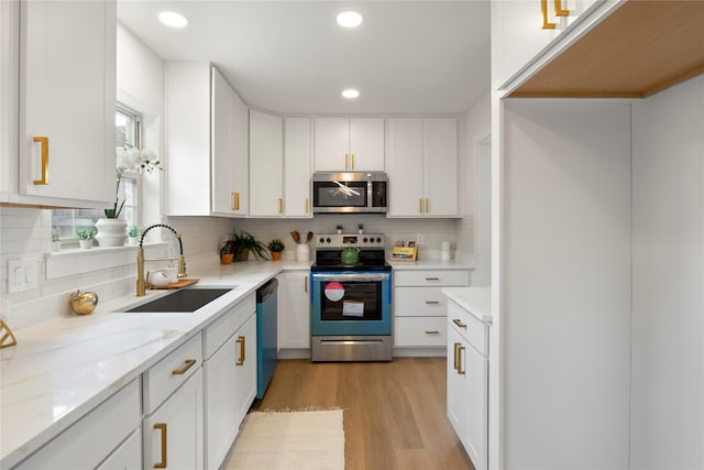 kitchen featuring recessed lighting, white cabinets, a sink, light wood-style flooring, and stainless steel appliances