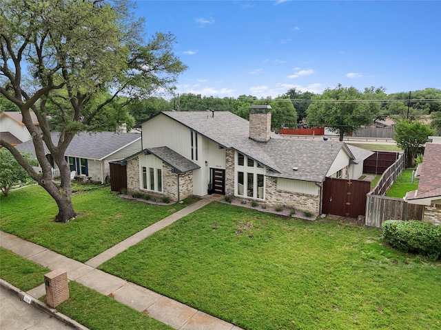 view of front of home featuring a chimney, roof with shingles, brick siding, fence, and a front lawn