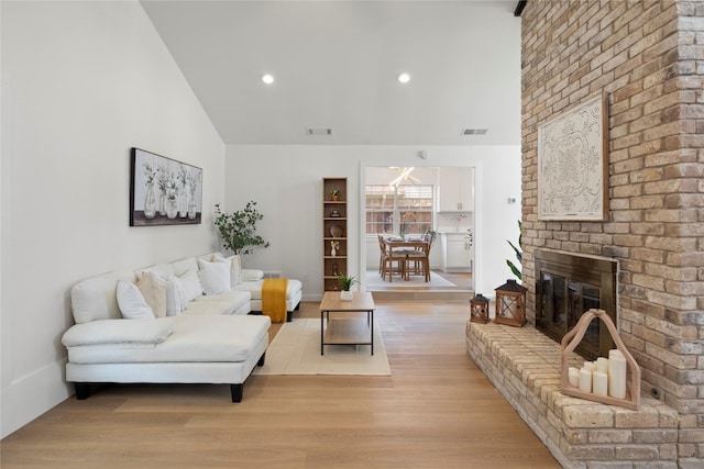 living room with visible vents, a fireplace, high vaulted ceiling, and light wood-type flooring