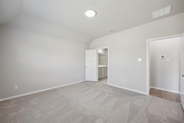 unfurnished bedroom featuring light colored carpet, baseboards, visible vents, and lofted ceiling