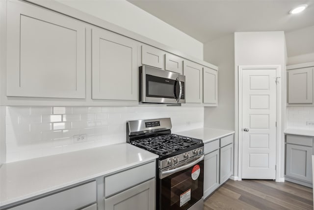 kitchen with gray cabinets, decorative backsplash, appliances with stainless steel finishes, wood finished floors, and light countertops