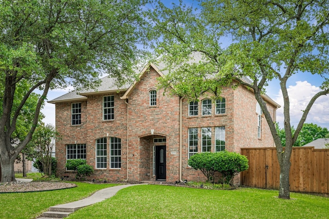 view of front facade with brick siding, fence, and a front yard