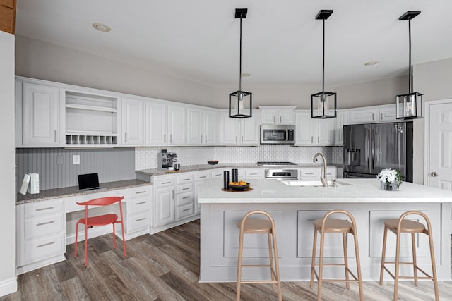 kitchen with open shelves, a sink, built in study area, stainless steel appliances, and wood finished floors