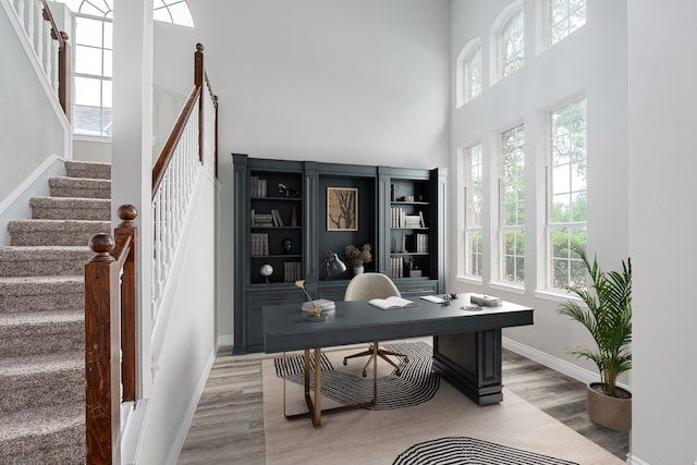office area with baseboards, light wood-style flooring, and a high ceiling