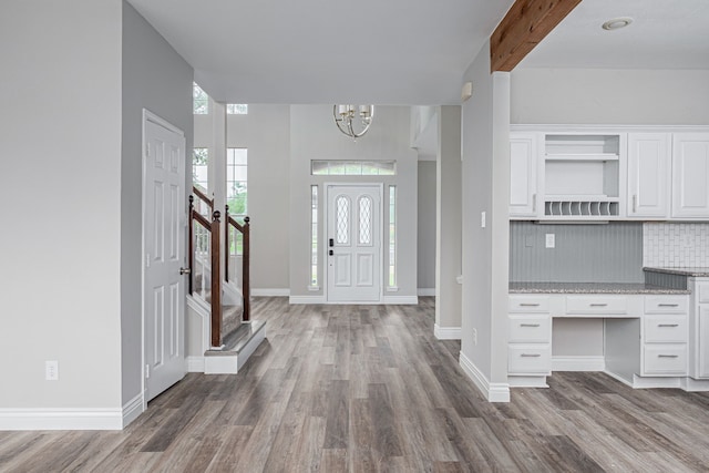 foyer featuring built in desk, wood finished floors, baseboards, a notable chandelier, and stairs