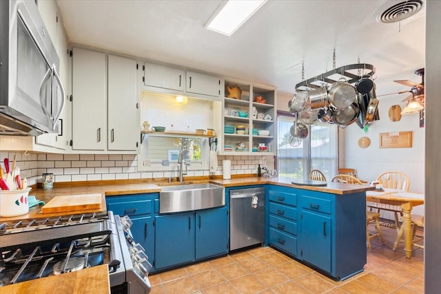 1324 Sunset St, Waco, TX 76710 - kitchen featuring blue cabinets, a sink, a peninsula, stainless steel appliances, and light tile patterned flooring