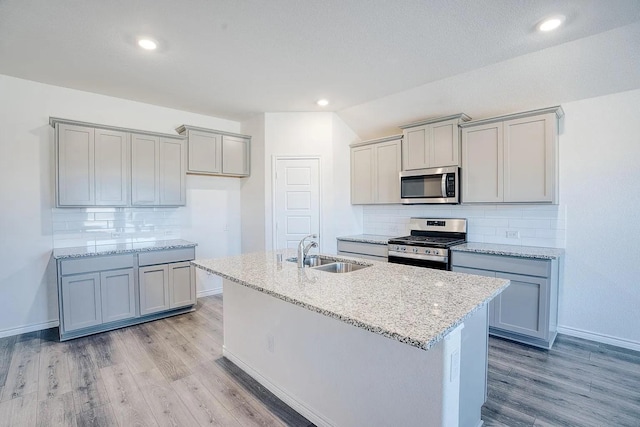 kitchen featuring a sink, appliances with stainless steel finishes, gray cabinets, and a center island with sink