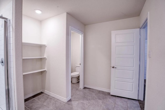 full bathroom with tile patterned flooring, toilet, a textured ceiling, baseboards, and a stall shower