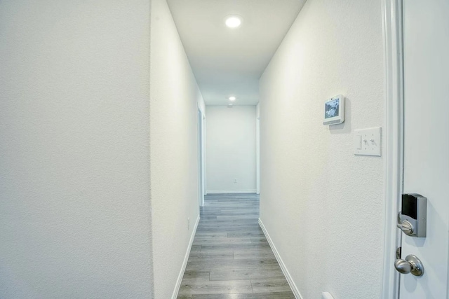hallway featuring baseboards, recessed lighting, a textured wall, and wood finished floors