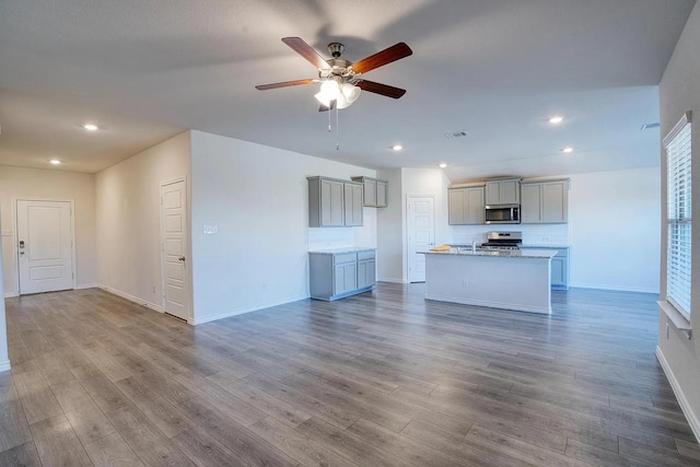unfurnished living room with a ceiling fan, baseboards, recessed lighting, and wood finished floors
