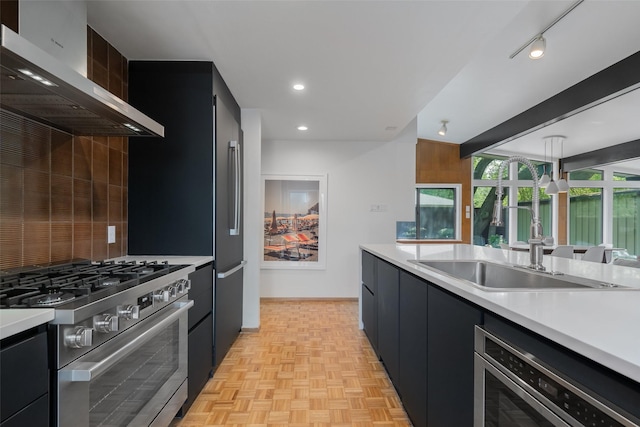 kitchen with wall chimney range hood, a sink, dark cabinetry, light countertops, and stainless steel appliances