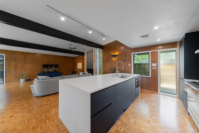 kitchen featuring visible vents, a ceiling fan, wooden walls, light countertops, and a sink