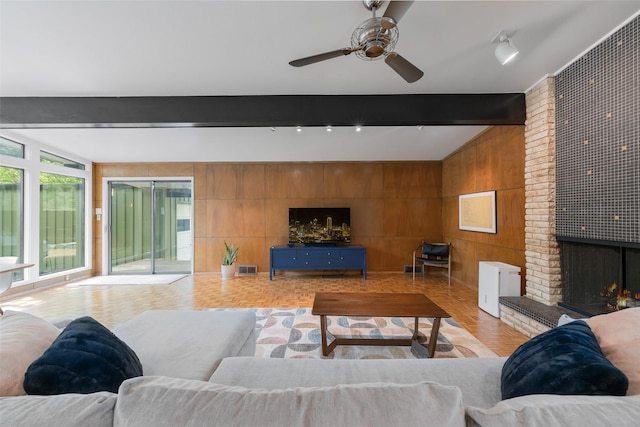 living room with visible vents, a fireplace, ceiling fan, wooden walls, and vaulted ceiling with beams