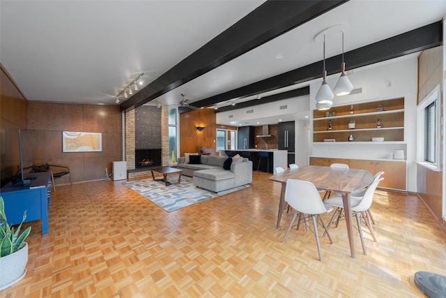 dining area featuring beam ceiling, wooden walls, a fireplace, and a healthy amount of sunlight