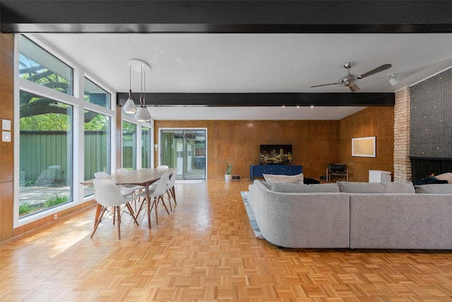 living area featuring lofted ceiling with beams, a ceiling fan, wood walls, and a brick fireplace