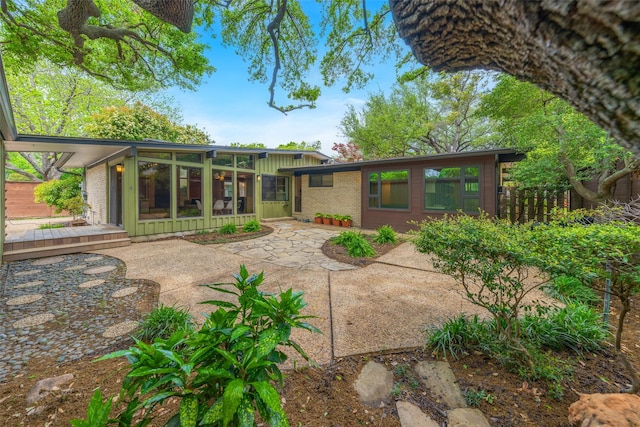 rear view of house featuring board and batten siding, a patio, brick siding, and a sunroom