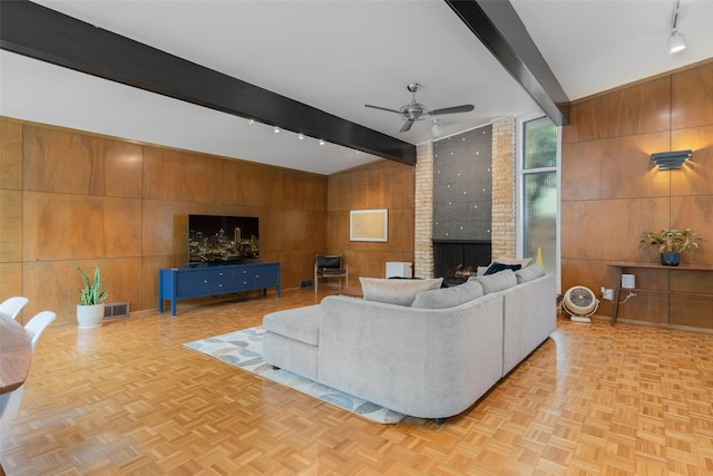 living room with track lighting, wood walls, visible vents, a brick fireplace, and ceiling fan