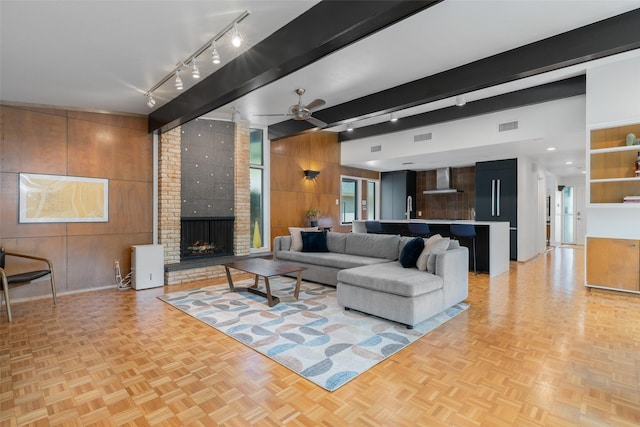 living room with track lighting, wood walls, visible vents, a fireplace, and ceiling fan