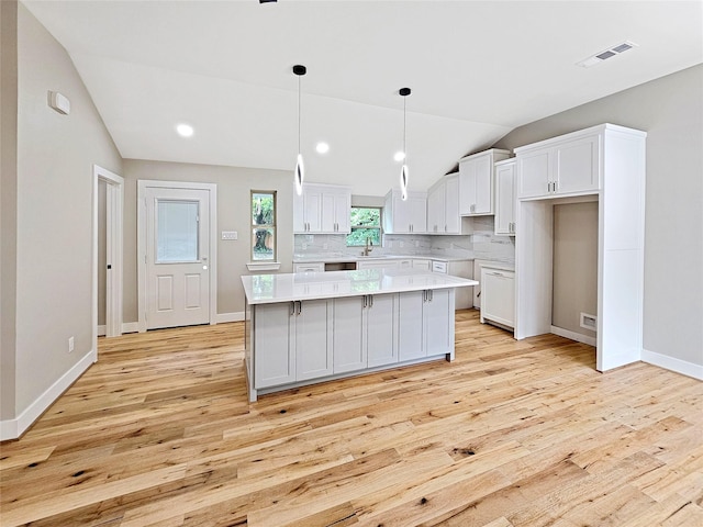 8622 Eden Valley Ln, Dallas, TX 75217 - kitchen with vaulted ceiling, light wood-style floors, white cabinets, decorative backsplash, and a center island