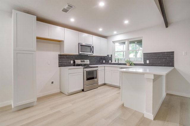 kitchen featuring decorative backsplash, visible vents, appliances with stainless steel finishes, a peninsula, and light wood-style flooring