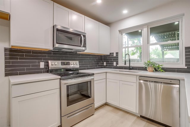 kitchen with light countertops, white cabinetry, a sink, appliances with stainless steel finishes, and backsplash